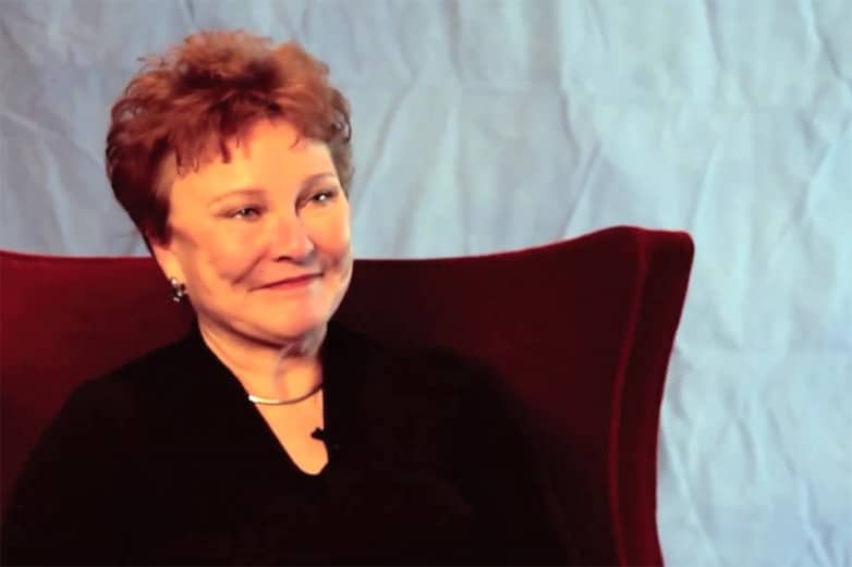 Woman with short auburn hair in a black top seated in a red chair during an interview
