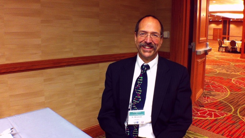 Man in a suit with a DNA-print tie and conference badge in a hotel ballroom