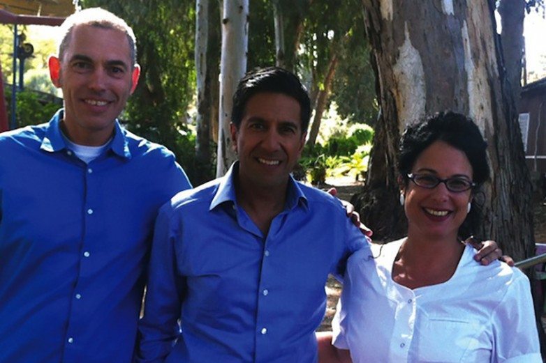 Dr. Sanjay Gupta posing between two colleagues outdoors beside a eucalyptus tree