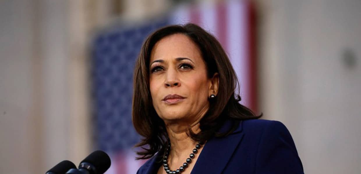 Kamala Harris speaking at a podium microphone before a draped American flag